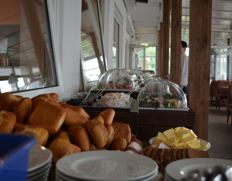 Frühstücksbuffet mit Brötchenkorb, dunklem Brot und gestapelten Tellern im Gastraum