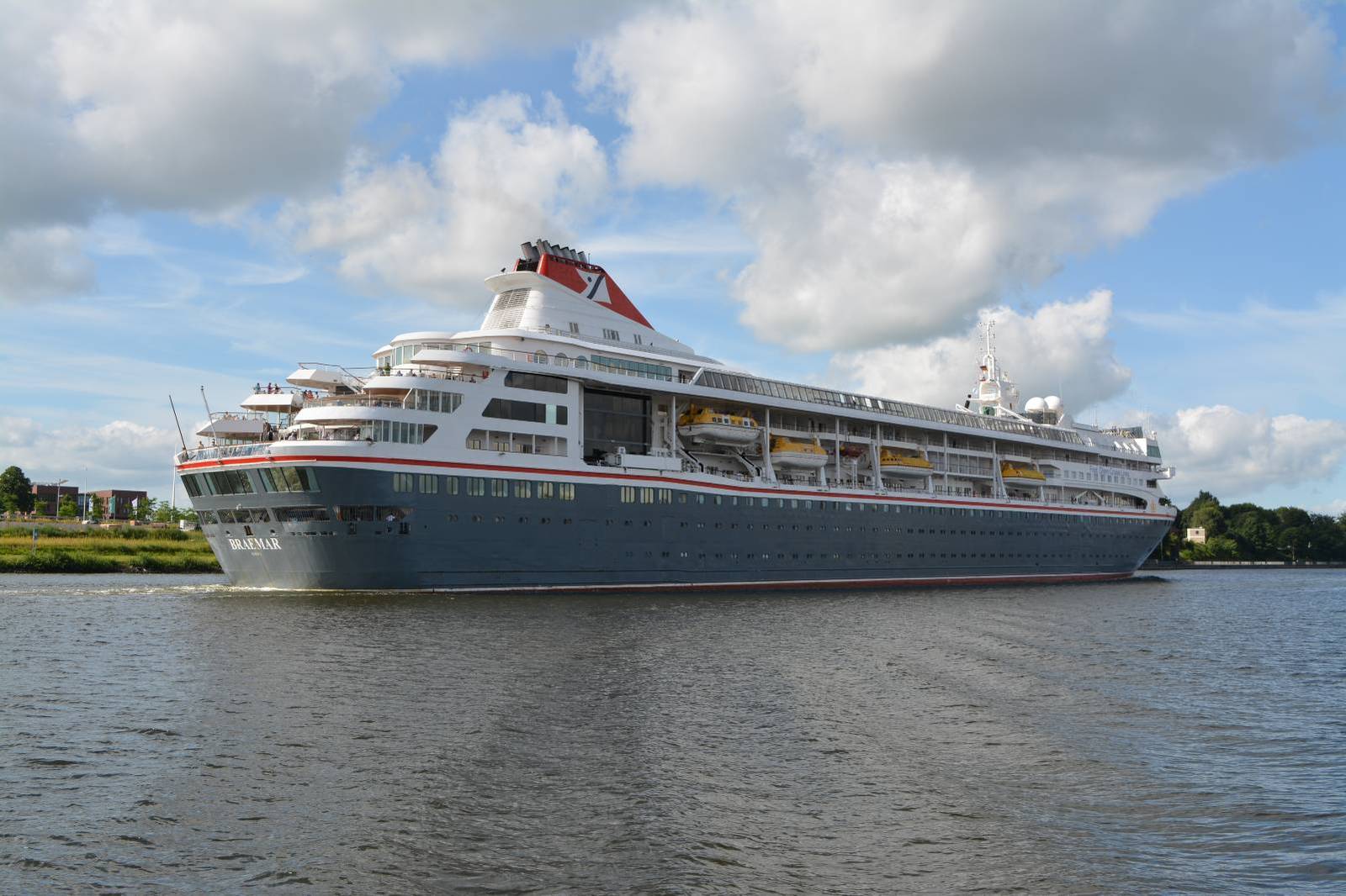Weißes Kreuzfahrtschiff zieht bei Sonnenschein am Ufer vorbei